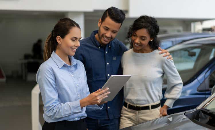 Saleswoman at a car dealership talking to a happy couple