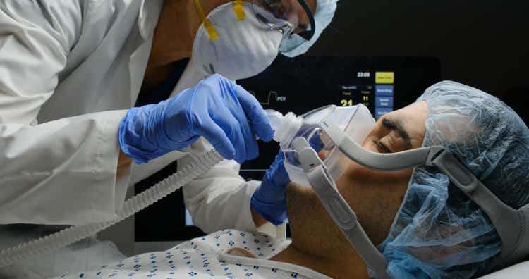 A doctor examines a patient with COVID-19 while she is connected to a ventilator