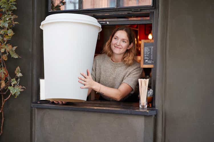 Smiling barista holding disposable coffee cup at take out counter of cafe