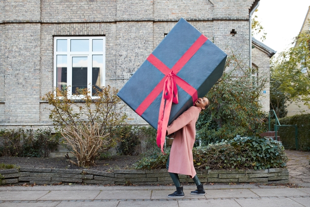 Happy woman carrying large gift box on footpath