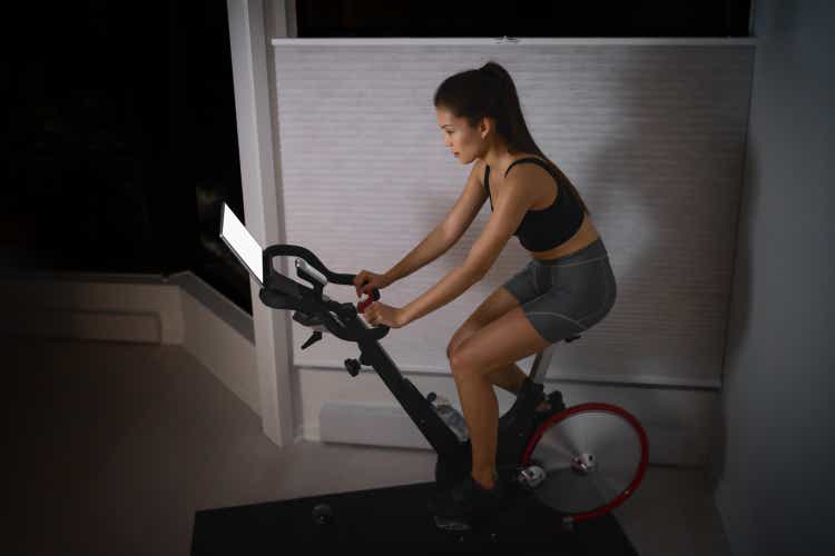 Home workout indoor stationary bike Asian girl biking screen with online classes woman training on smart fitness equipment indoors for cycling exercise. Late at night in bedroom