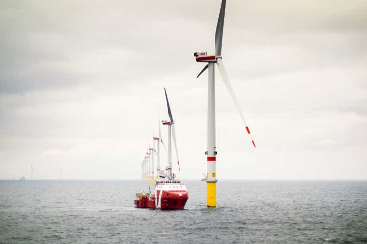 The large transport ship Normand Jarstein standing at Orsted's wind farm Borkum Riffgrund 2. The wind turbines are in a row behind the ship. Sky is moody.