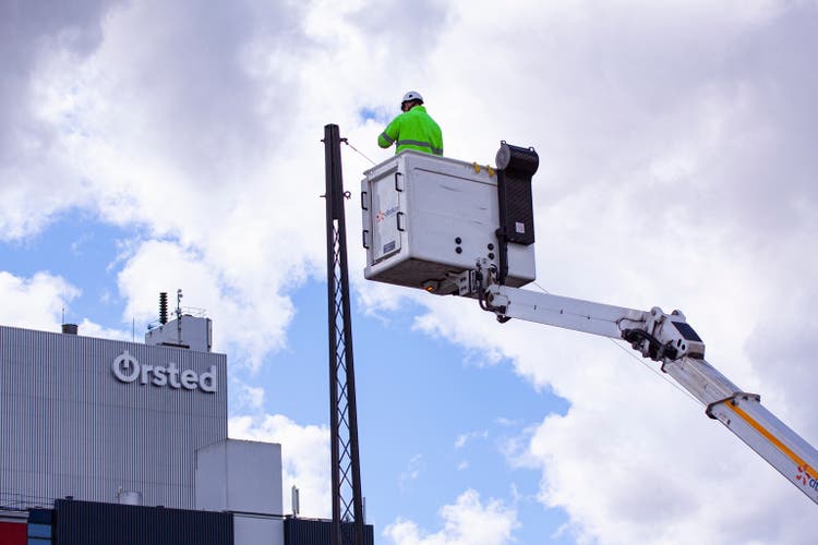 Lineworker working on power lines in crane bucket woth Ørsted logo on building.