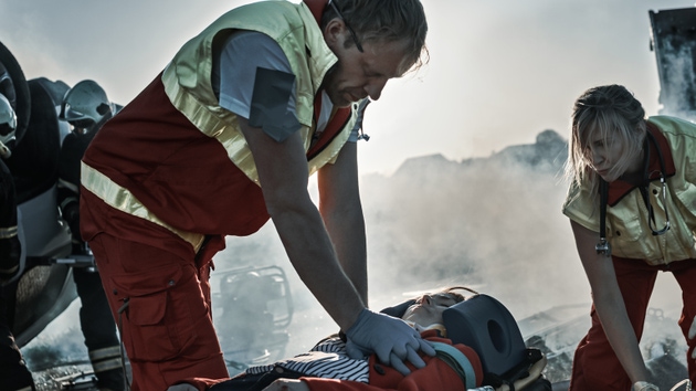On the Car Crash Traffic Accident Scene: Paramedics Saving Life of a Female Victim who is Lying on Stretchers. They Apply Oxygen Mask, Do Cardiopulmonary Resuscitation / CPR and Perform First Aid