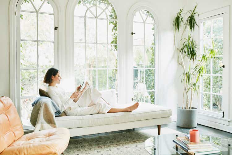 Woman sitting on couch in living room reading on digital tablet