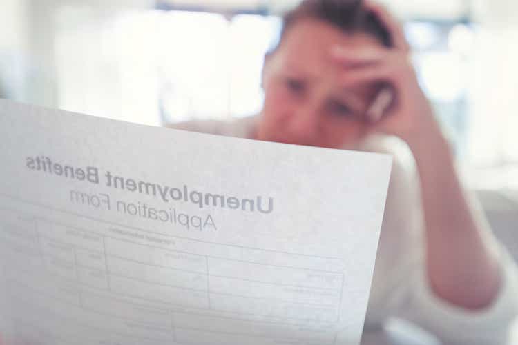 Woman looking worried holding an unemployment benefits application at home.