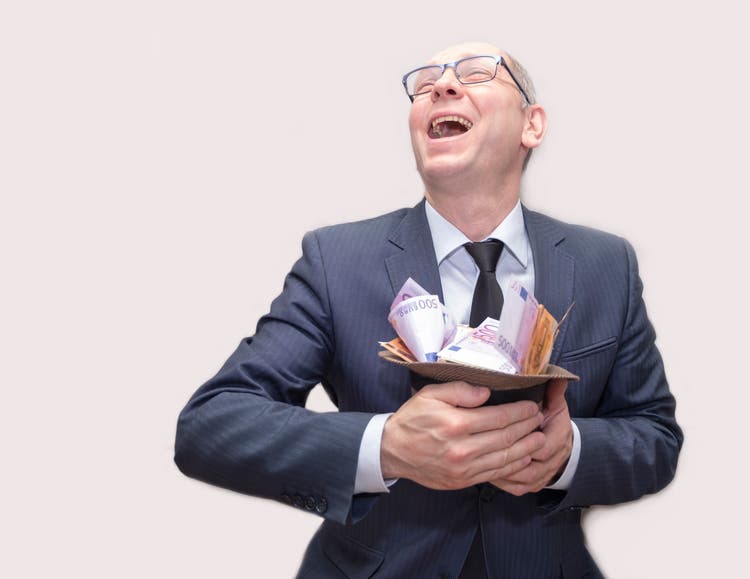 The man is laughing happily. A man in a suit and glasses holds a hat in his hands and a lot of money and enjoys wealth.