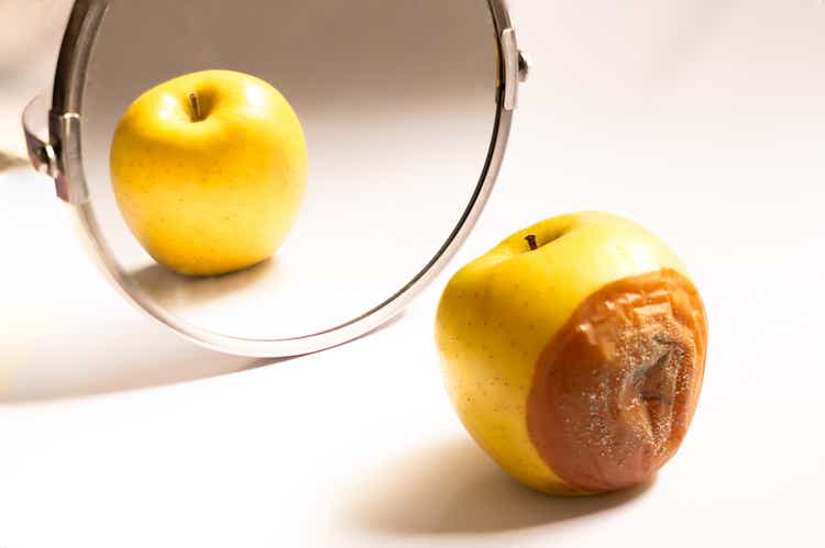 Apple in good condition looking at itself in the mirror while its back is rotten. Deception