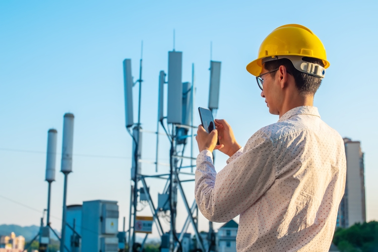 Engineer holding mobile phone testing the communications tower