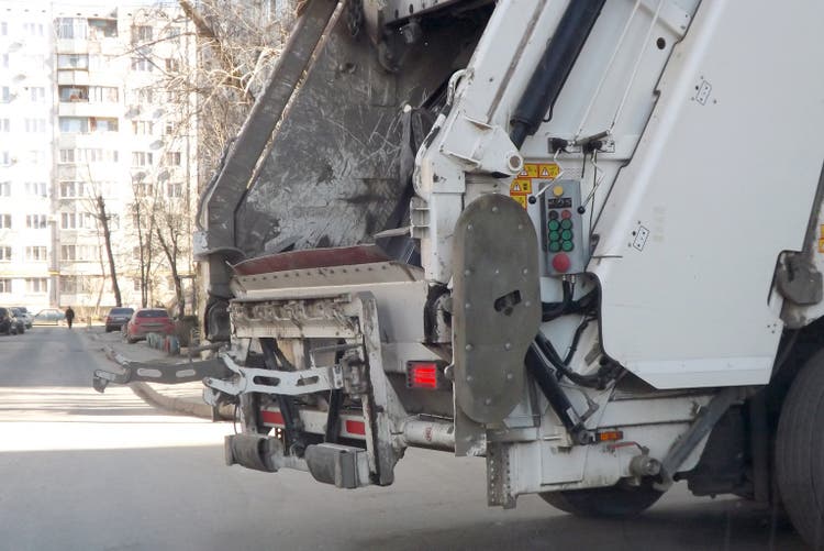 The back of the garbage truck prepares to take in garbage bins inside. Garbage collection in the courtyards of residential buildings. Close-up.