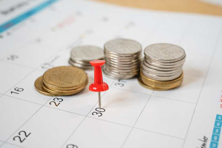 red pin marked on the end of month of calendar with blurred coins, business and finance background