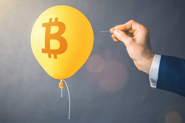 Bitcoin cryptocurrency symbol on yellow balloon.  Man holds needle aimed at hot air balloon.  The concept of financial risk