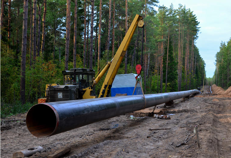 Pipelaying crane lowers a section of pipe into a trench. Construction of gas pipeline to new LNG plant. Crawler bulldozer with side boom operation install natural gas pipeline and oil pipes