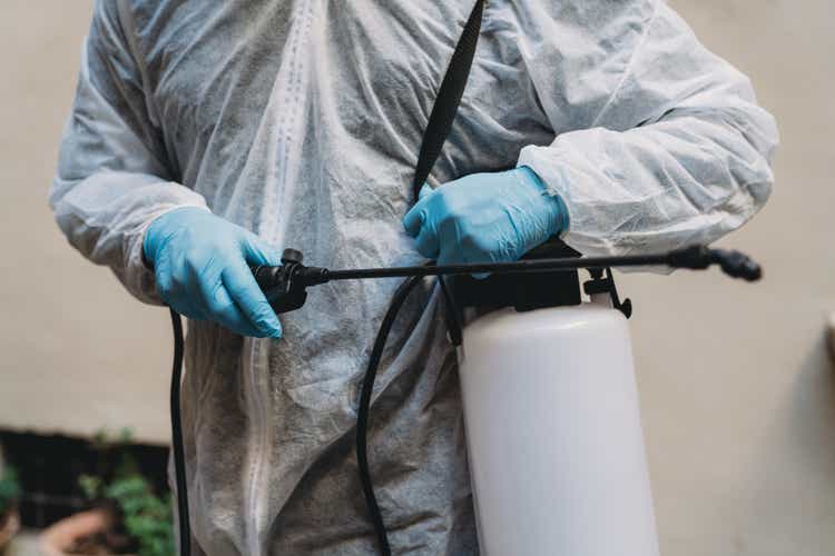 Detail of a sanitation worker in protective suit holding a sprayer