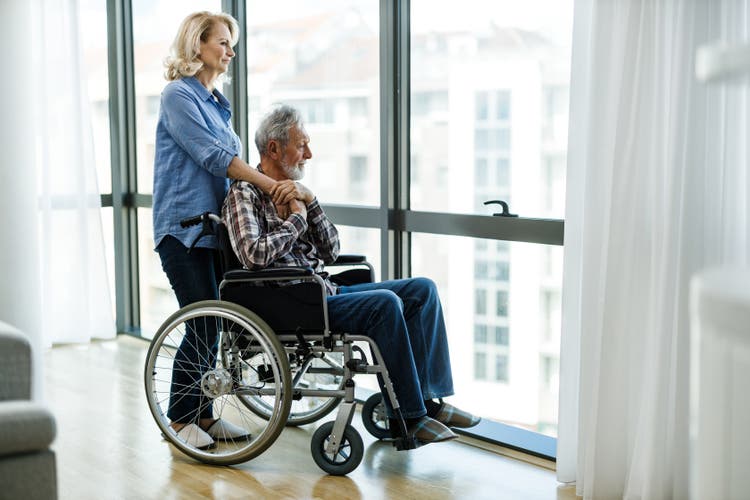 Mature woman and her disabled husband looking through window.