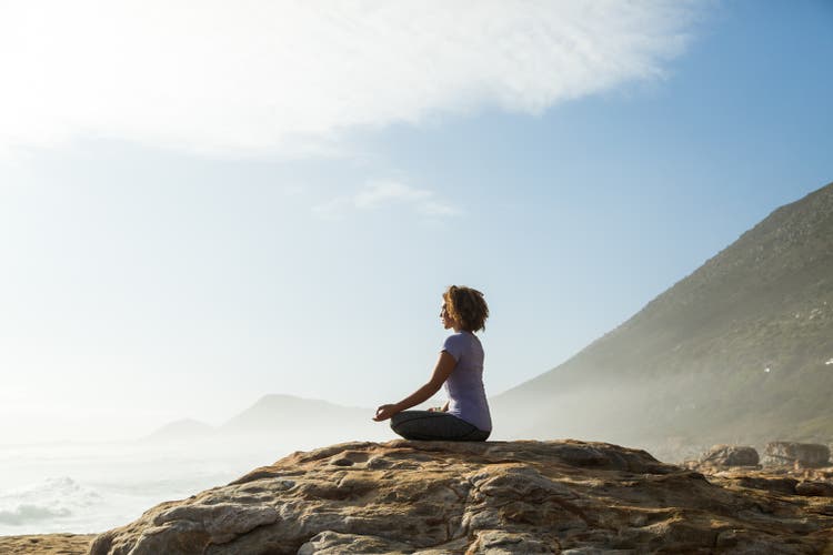 Woman meditating on rock by the sea