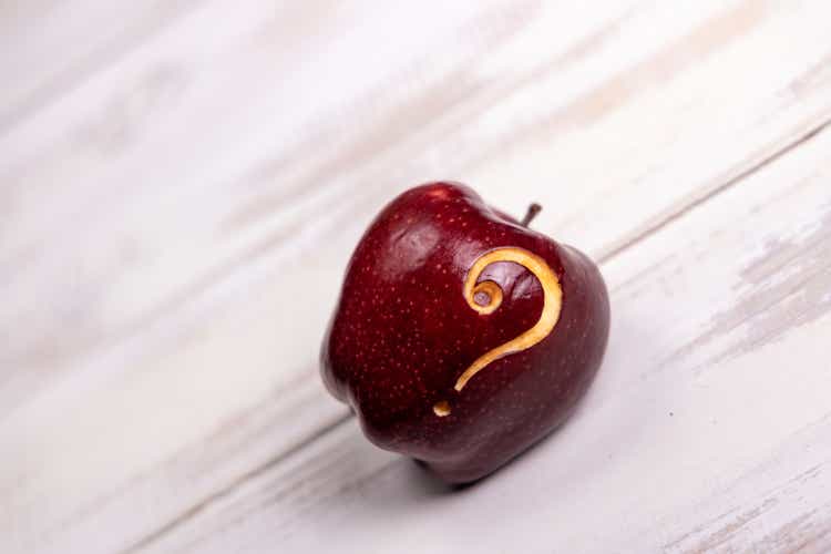 Ripe red apple with a question mark carved into it and placed on plain timber table with copy space - creative stock image