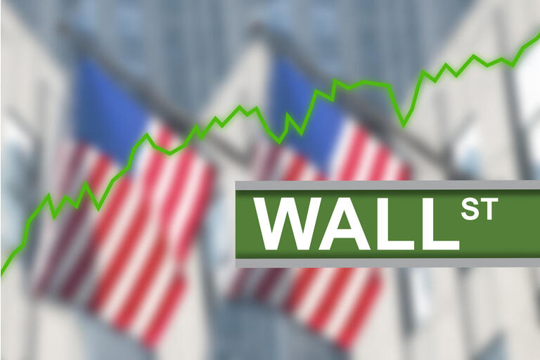 Wall Street sign post with green line chart diagram indicating stock market going up. In the background blurred American US flags hanging from buildings