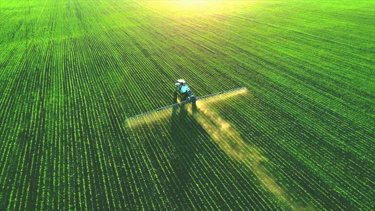 Tractor sprays fertilizer on lush green fields.