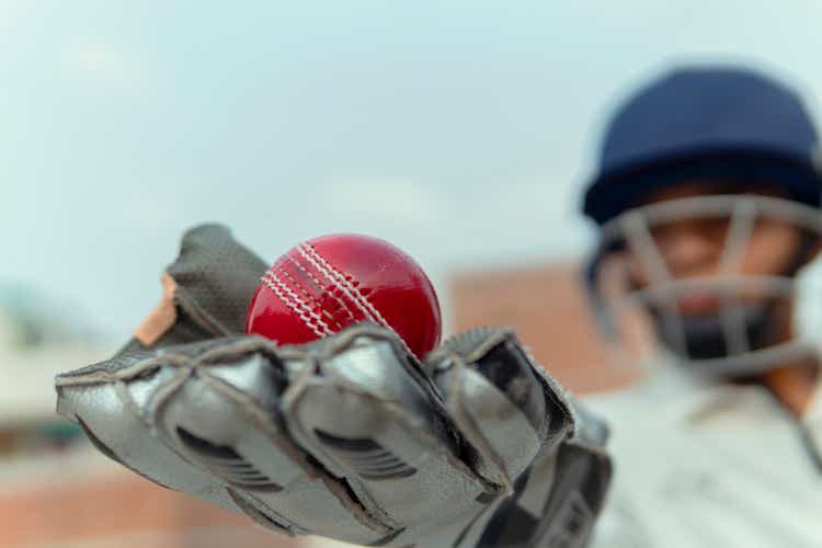 A boy in cricket uniform and wearing keeper gloves with hold leather ball. and doing practice