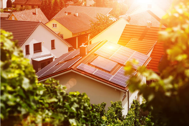 Solar panels on the tiled roof of the building in the sun. Top view through grape leaves. Image for illustration on energy, self-reliance, autonomy and security.