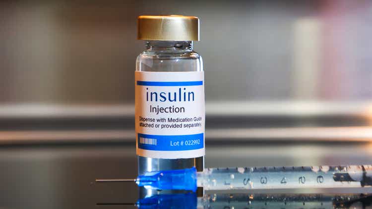 Vial of insulin injection with a syringe on black table and stainless steel background.