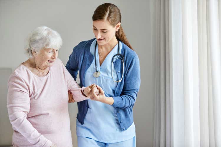Nurse assisting elderly female in walking at home