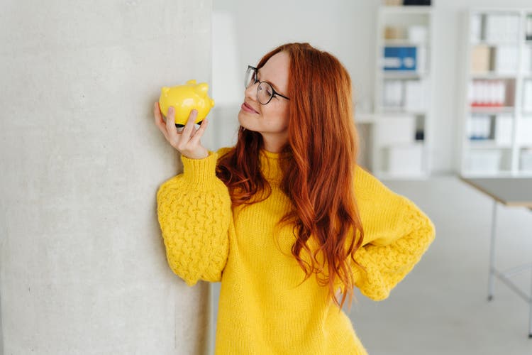 Smiling young woman contemplating a piggy bank