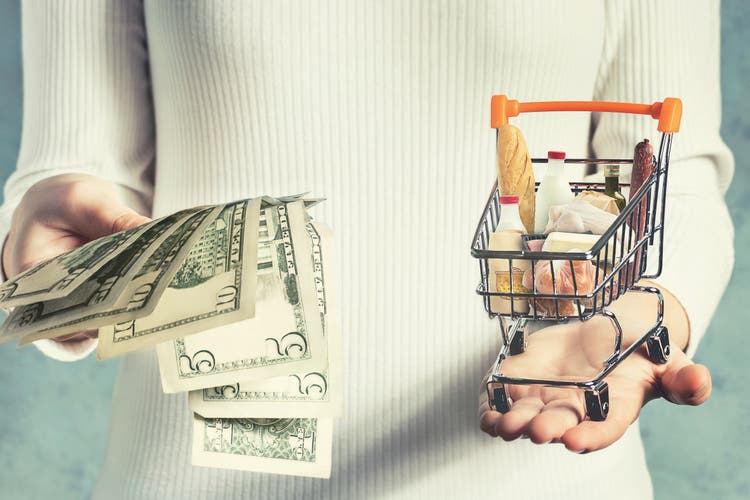 Consumer basket value concept. Girl weighs money and a shopping basket in her hands