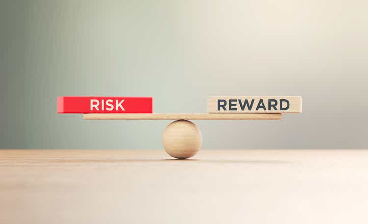 Wooden Seesaw Scale and Risk and Reward Written Wooden Blocks Sitting on Wood Surface in Front of Defocused Background