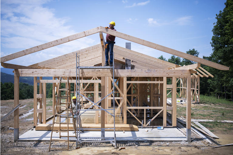 Construction Workers Working On Wooden Roof Of House.