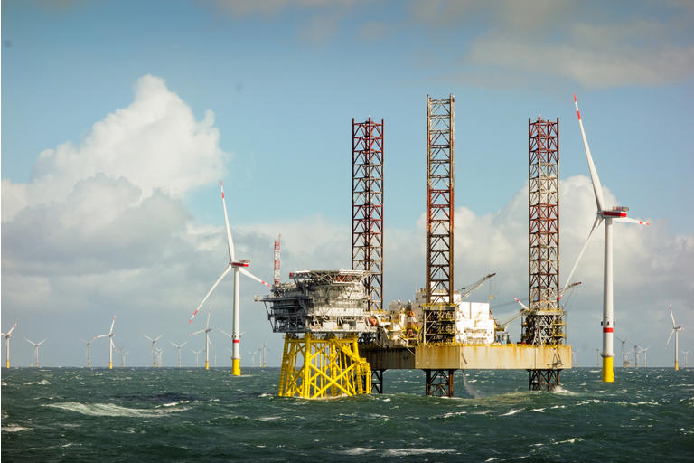Epic view on Large offshore 8MW wind turbines, wind farm on the horizont in north sea with jack up boat and offshore platform in wavy sea
