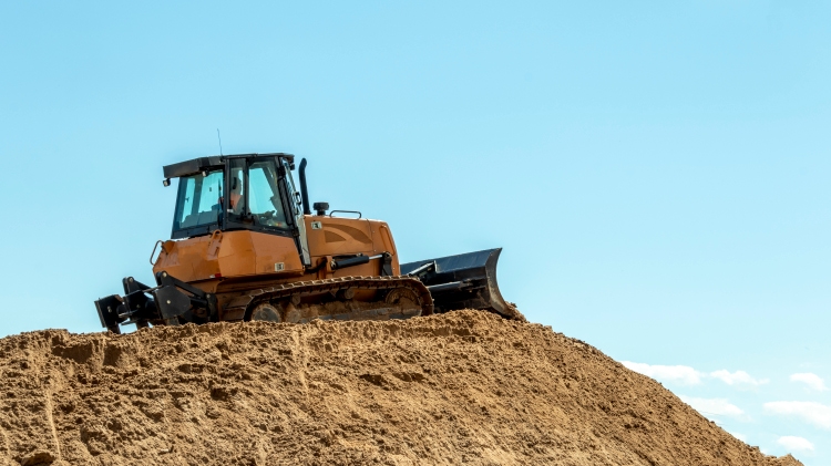 a bulldozer on a large pile of sand against a blue sky