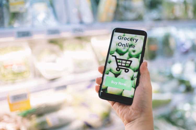 online shopping mobile app holding by a hand with blurred background of supermarket grocery on a mobile screen