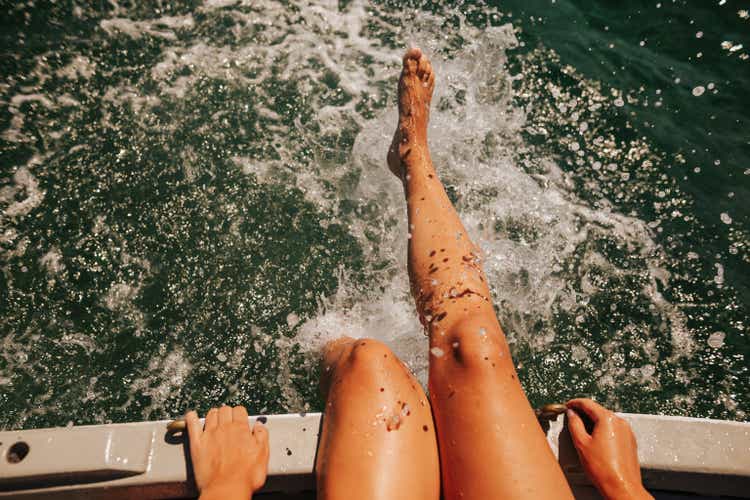 Young woman sitting on a boat and splashing on the water