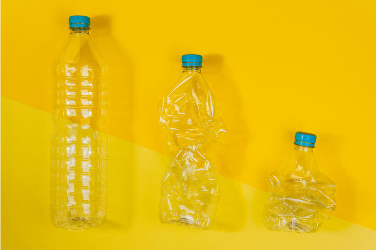 Transparent and crushed plastic bottles with blue caps on a yellow background. Recycling and environment concept.