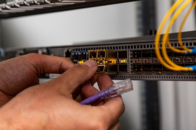 The electrician inserts the SFP module into the router and holds the patch cord. Hands in the frame. Small form-factor pluggable transceiver. Horizontal orientation