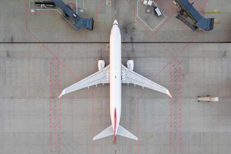 Top down view on comercial airplane docking in terminal in the parking lot of the airport apron, waiting for services maintenance, refilling fuel services after airspace lock down. Modern airliner