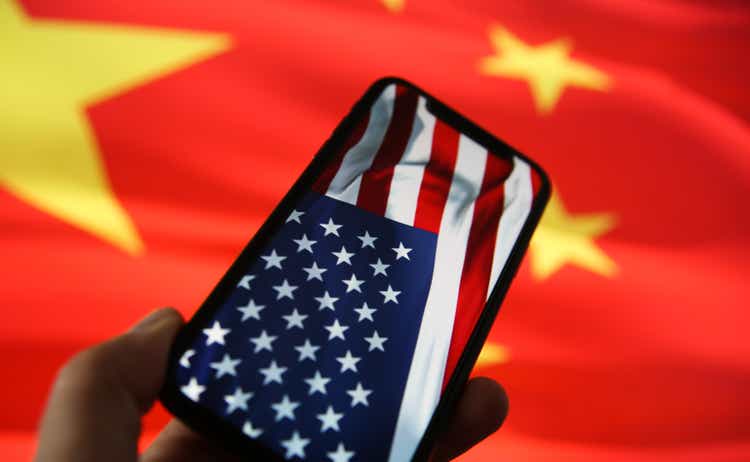 Chinese american economic relationship concept: View on hand holding mobile phone with USA flag. Blurred flag of China background