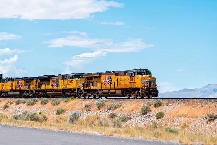 Utah Landschaft mit Zug auf der Eisenbahn mit Autos Container, und amerikanische Flagge