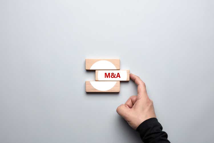 M&A merger and acquisitions concept. Male human hand pushing the wooden block with the word M&A and completing the merger process.