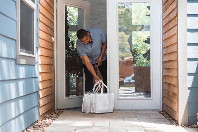 Man retrieves groceries from front porch after contactless delivery