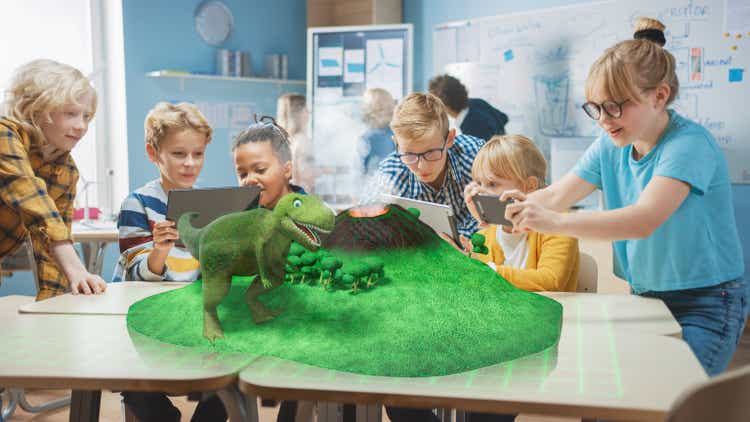 Groupe d'enfants d'école utilisent des ordinateurs tablette numérique avec l'application de réalité augmentée, regardant l'animation 3D éducative - Dinosaur Walking on Island avec Volcan actif. VFX, Rendu des effets spéciaux