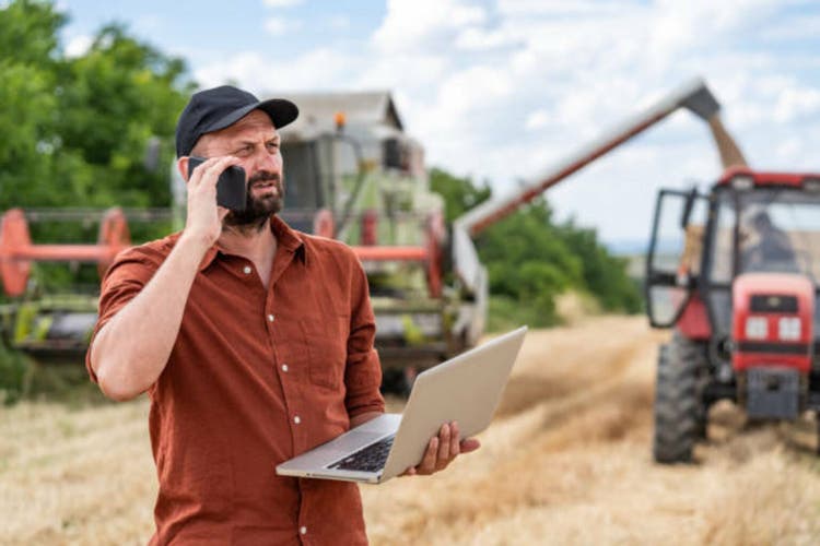 Farmer controlled harvest in his field talking on a smart phone and using laptop