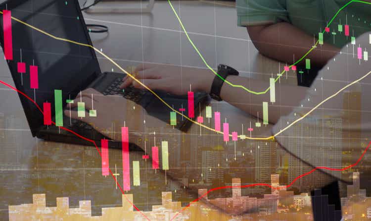 double exposure of stock graph chart candle stick and stock trader using laptop on desk, city night view on background, stock trader and graph analysis concept