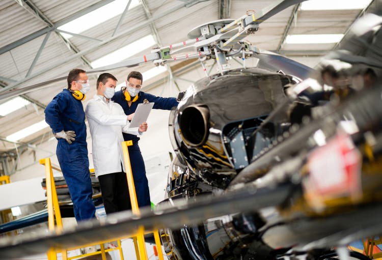 Group of mechanics wearing facemasks at work while doing an inspection on a helicopter