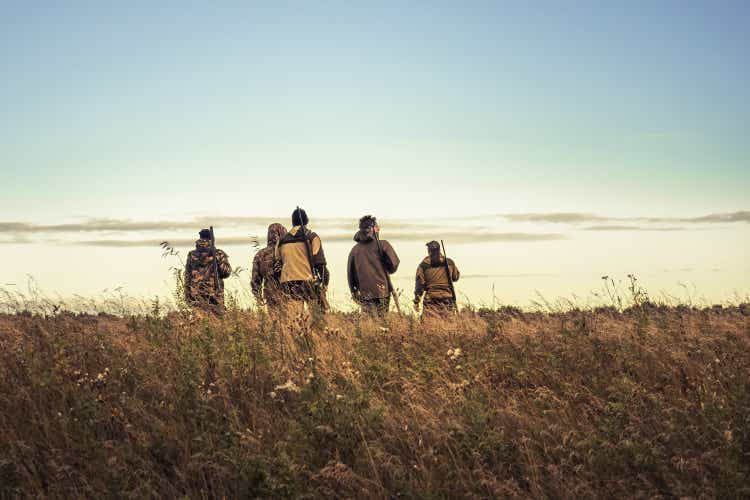 Hunters silhouettes against sky going through rural field towards horizon during hunting season