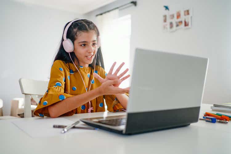 Teenage girl with headphones and laptop having online school class at home