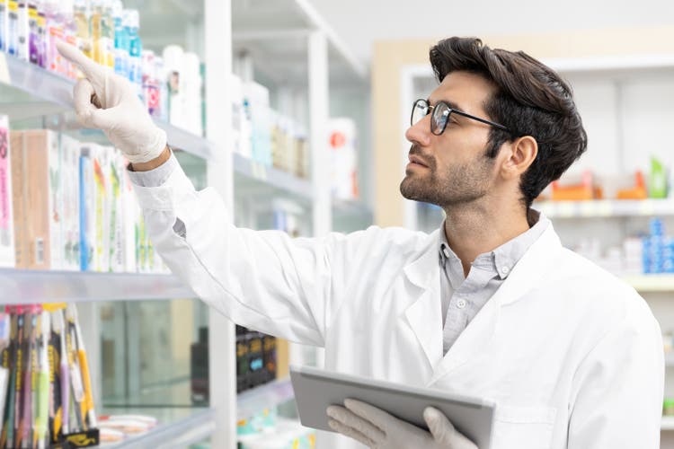 Farmacéutico masculino que revisa la farmacia de stock utilizando la tecnología de tabletas digitales en farmacia moderna.