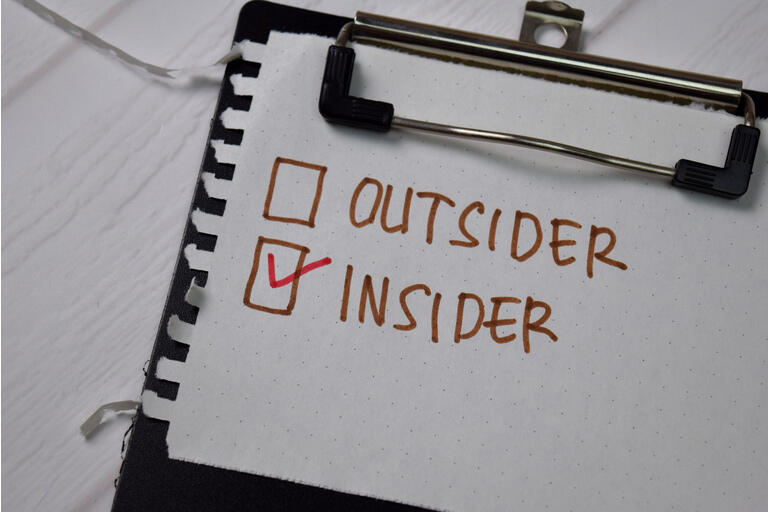 Outsider and Insider write on a sticky note. Supported by an additional services isolated wooden table.